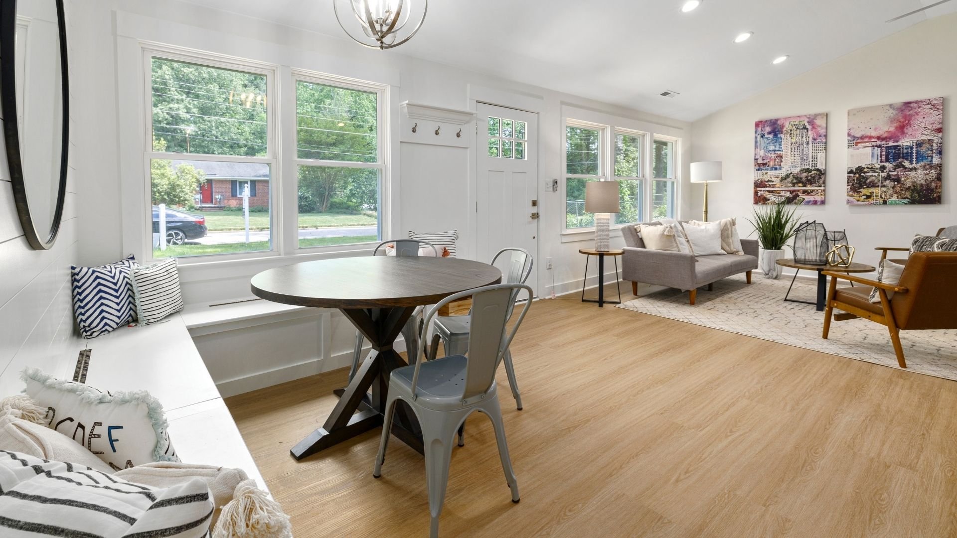 Modern open-concept living and dining room with round table, sofa, large windows, and natural wood flooring.