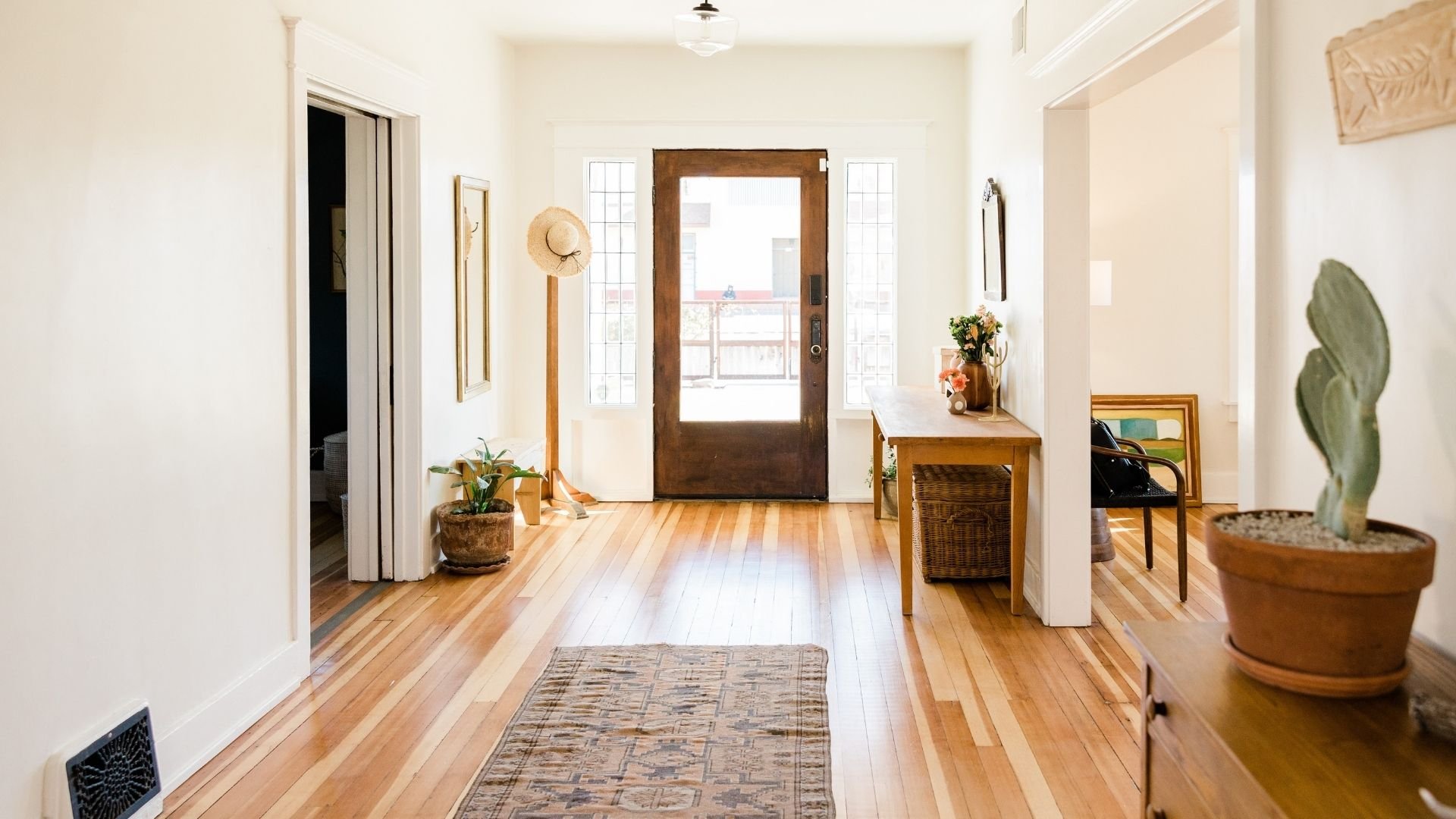 Bright, minimalist entryway with wooden floors, door leading to balcony, potted plants, and woven décor.