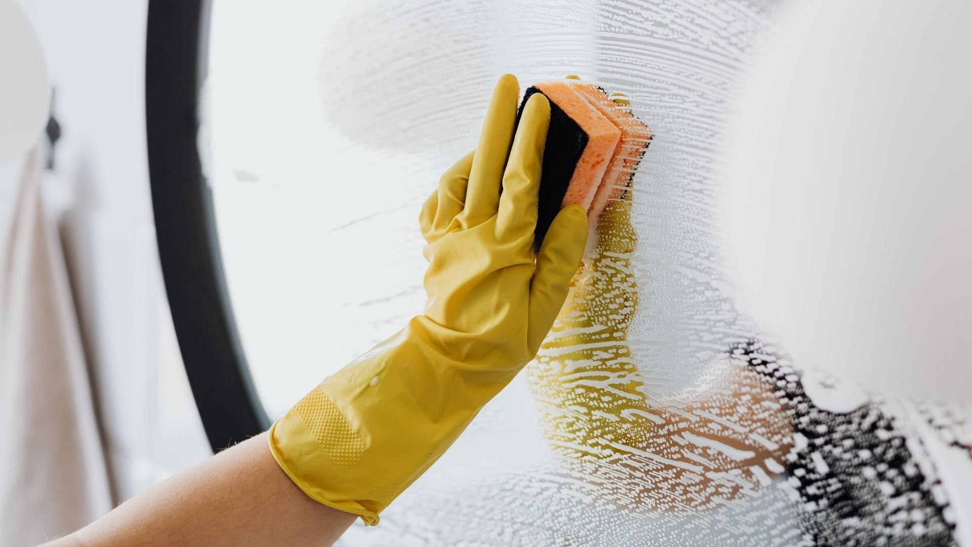 Hand in yellow glove holding orange brush cleaning white textured wall surface