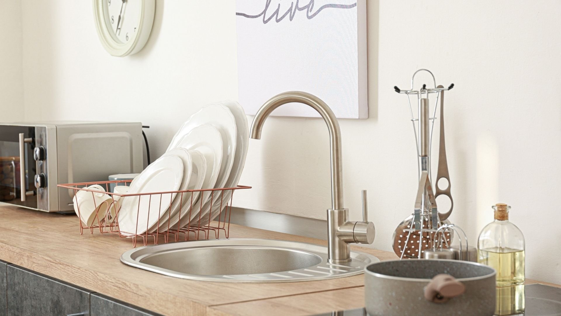Modern kitchen sink with metal faucet, drying rack with white plates, and kitchen accessories