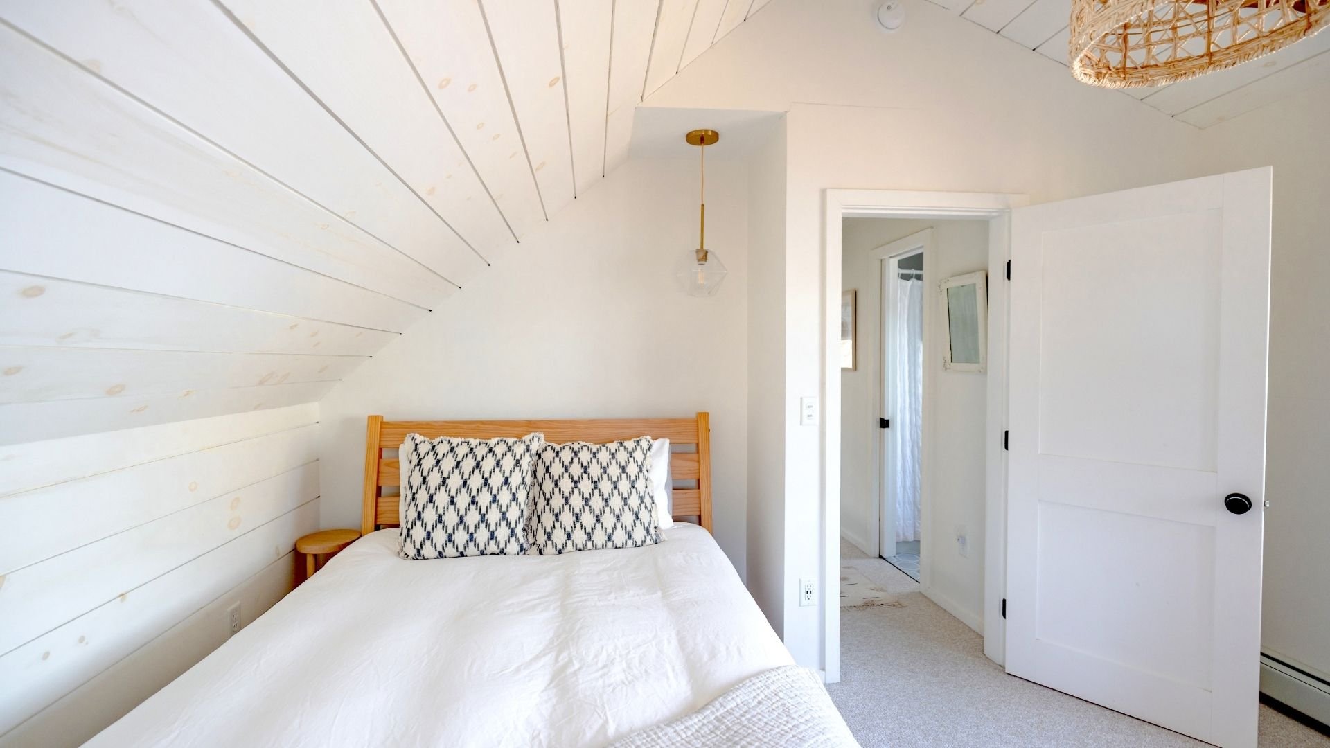 Bright, minimalist bedroom with white shiplap walls, wooden bed, and pendant light.