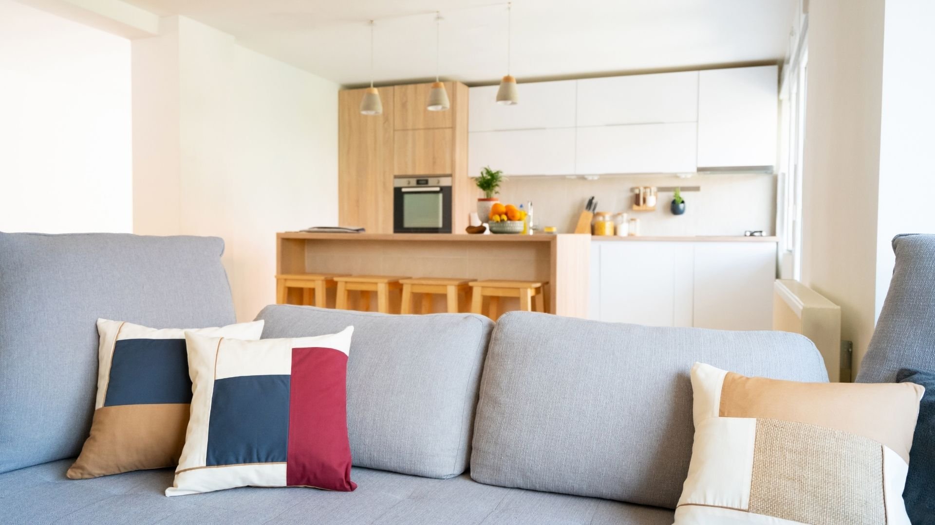 Modern studio apartment with gray sofa, wooden kitchen, white cabinets, and pendant lighting